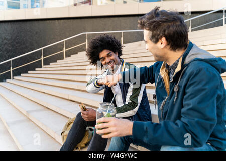 Two happy casual businessmen sitting on stairs having lunch break Stock Photo