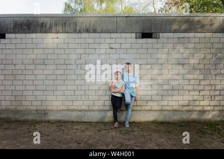 Portrait of two girls standing at a brick wall Stock Photo