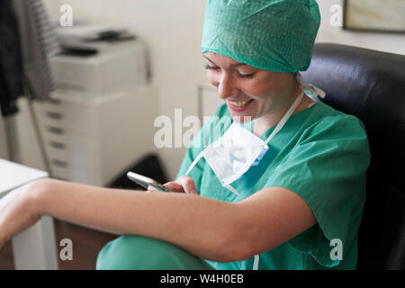 Happy woman in scrubs having a break using cell phone Stock Photo