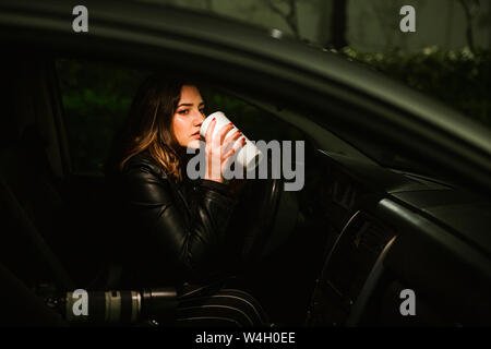 Young woman with disposable cup and camera in a car at night Stock Photo