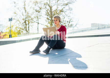 Portrait of young freelancer sitting outdoors using digital tablet and headset Stock Photo