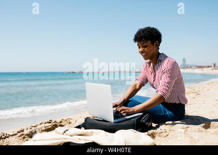 Woman sitting on the beach while working with the laptop Stock Photo