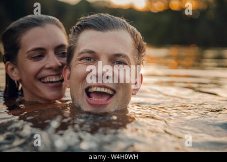 Young couple swimming in lake at sunset