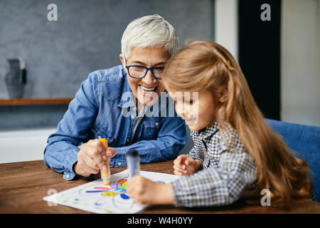Grandmother and granddaughter sitting at table, painting colouring book Stock Photo