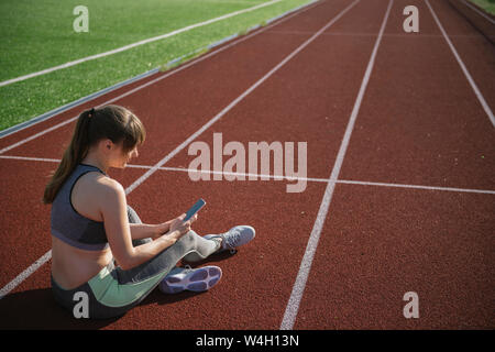 Sportswoman sitting on racetrack using smartphone Stock Photo