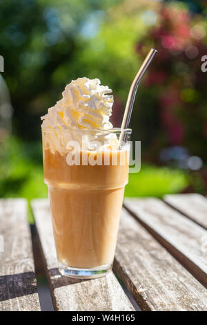 Glass of iced coffee with cream topping on garden table Stock Photo