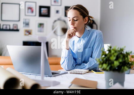 Woman with closed eyes in office with wind turbine model on table Stock Photo