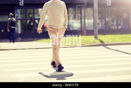 senior man walking along city crosswalk Stock Photo