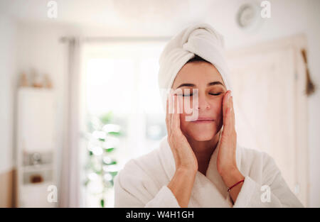 Portrait of mature woman in a bathroom at home applying moisturizer Stock Photo