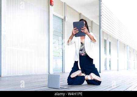 Female balett dancer kneeling on the ground, using tablet Stock Photo