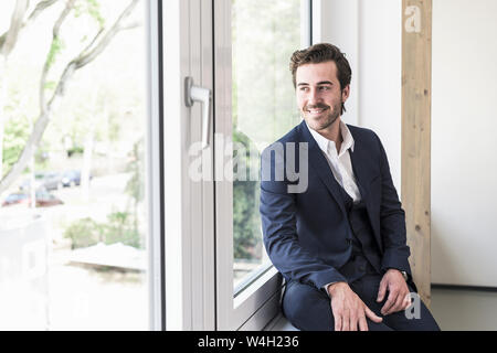 Young businessman sitting on the windowsill, smiling Stock Photo