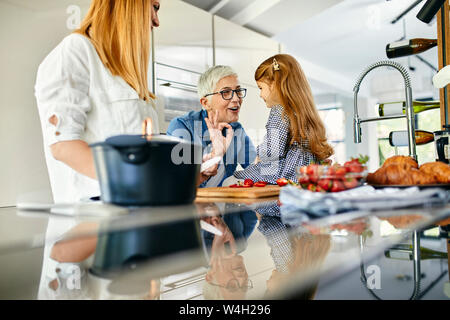 Mother, daughter and grandmother having fun, chopping strawberries in the kitchen Stock Photo