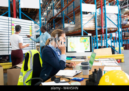 Female manager talking on mobile phone at desk Stock Photo