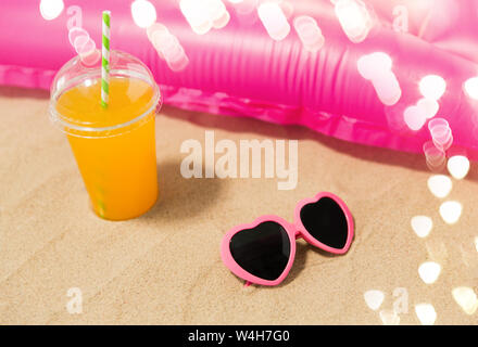 sunglasses, juice and pool mattress on beach sand Stock Photo