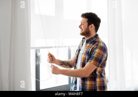 man opening roller blind on window at home Stock Photo