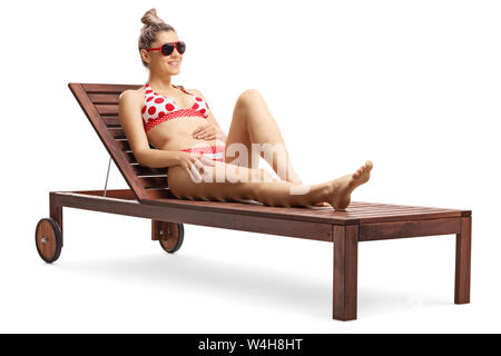 Full length shot of a young blond attractive woman in bikini sitting on a sunbed isolated on white background Stock Photo