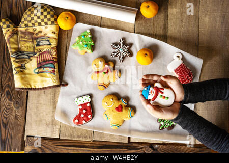 Ginger Christmas glazed gingerbread cookies on a wooden table. The child holds a gingerbread snowman in his hands. View from above. Stock Photo