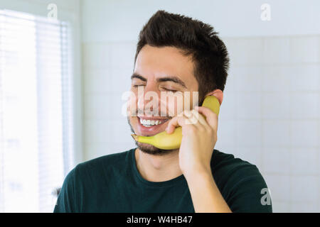 A young handsome brunette man is talking on the phone, instead of using a banana. Conceptual photo. Stock Photo