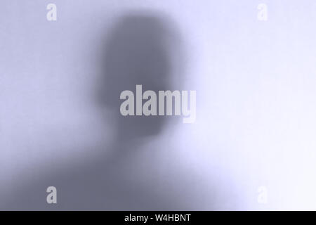 Blurred scary ghost face behind a white glass background. Horizontal orientation Stock Photo