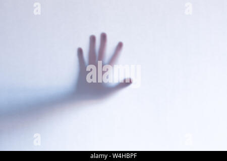 Blurred scary ghost hands behind a white glass background. Horizontal orientation Stock Photo