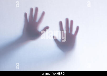 Blurred scary ghost hands behind a white glass background. Horizontal orientation Stock Photo