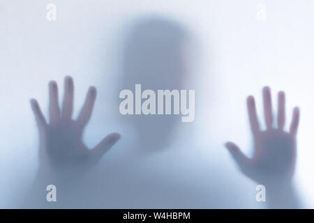 Blurred scary ghost silhouette behind a white glass background. Horizontal orientation Stock Photo