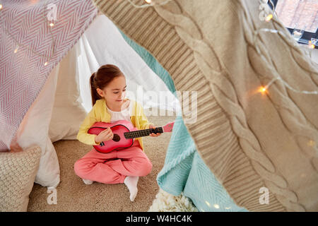 little girl playing guitar in kids tent at home Stock Photo