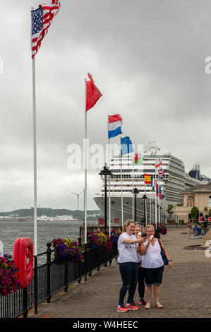 Female tourists taking a selfie in John F. Kennedy park at the Cobh cruise terminal as the MSC cruise ship liner docking in background, Cobh, County Cork, Ireland Stock Photo
