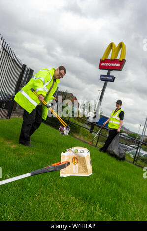 Close up of litter picker holding fast food wrapper with two people and a McDonalds sign in the background Stock Photo