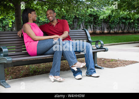 Happy young couple sitting on a wooden bench in an inner city park. Stock Photo