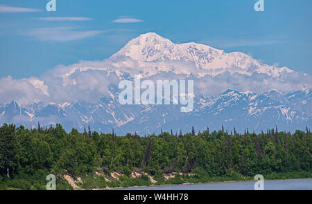 closeup view of Denali peak in the Alaska Range with a forest and lake in the foreground blue sky and small clouds in the background Stock Photo