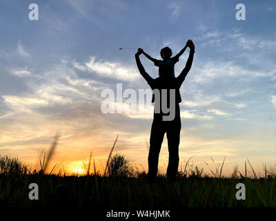 Silhouette Father Carrying Son Against Sky During Sunset. Stock Photo
