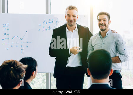 Smiling adult men in formal suits standing near whiteboard doing presentation for coworkers in modern light office Stock Photo