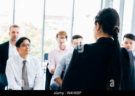 Back view of stylish woman giving presentation for male colleagues working together in office Stock Photo