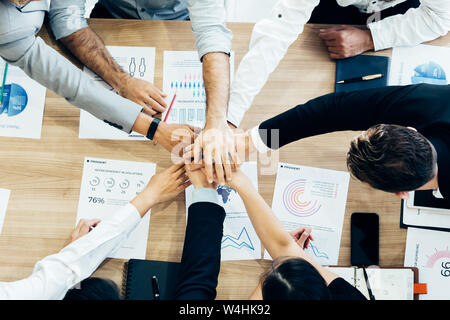 Crop coworking business people stacking hands above wooden desk with paper documents Stock Photo