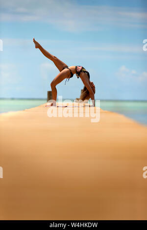 Woman bends over backwards while doing yoga on a pier. Stock Photo