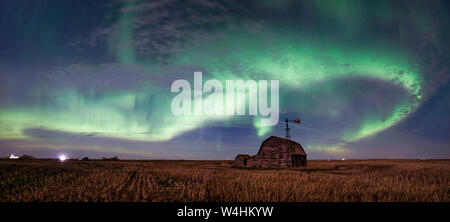 Swirl of bright Northern Lights over vintage barn, bins, windmill and stubble in Saskatchewan, Canada Stock Photo