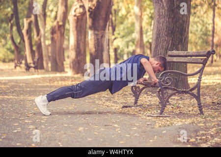 Picture of a young athletic man doing push ups in the park, preparing for morning workout. Stock Photo