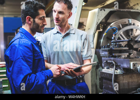 Two workers discussing a project in front of CNC lathe machine Stock Photo