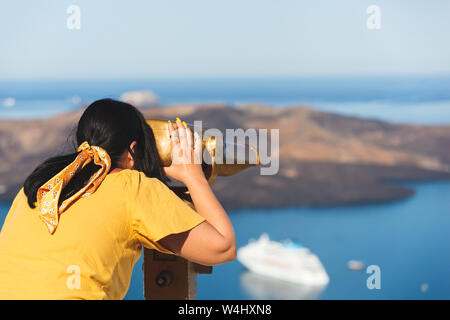 Beautiful young woman looking at cruise ships with binoculars in Thira, Santorini, Greece  enjoying vacation, selective focus