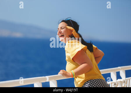 Happy Woman On A Cruise Vacation. standing on deck of cruise ship, strong wind blowing her hair Stock Photo