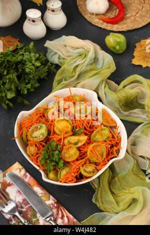 Korean-style salad with green tomatoes and carrots in a white salad bowl on a dark background, vertical photo Stock Photo