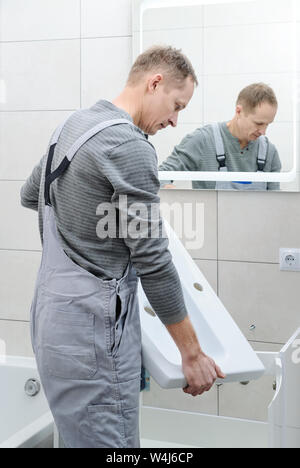 The man is setting the washbasin over the cabinet in the bathroom. Stock Photo