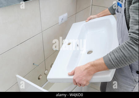 A man is setting the washbasin over the cabinet in the bathroom. Stock Photo