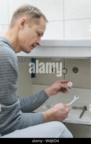 The man is setting a washbasin in the bathroom. He is holding the wrench. Stock Photo