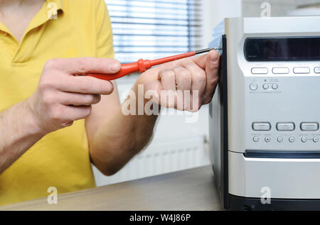 The man is using a screwdriver to open the music system. Stock Photo
