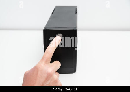 The index finger is pressing the start button of the uninterrupted power supply. Stock Photo