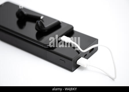 There is a smartphone, a wireless headset and a power bank with charging cable on a white background. Stock Photo