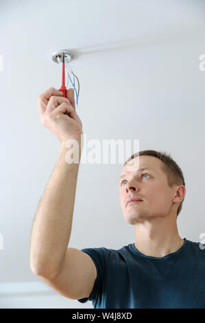 Installing a spotlight in the room. The man is fixing the bracket for the ceiling lamp. Stock Photo