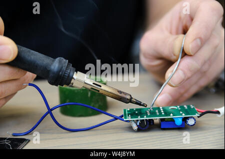 The man is repairing the power supply of the lamp. He is holding an electronic board and a soldering iron. Stock Photo